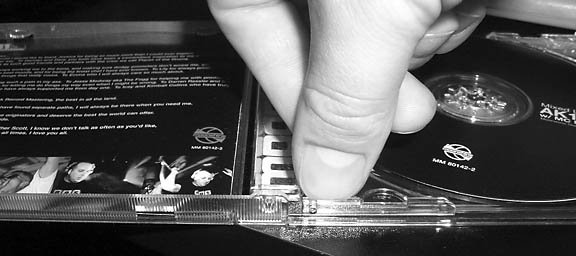 A thumbnail squeezed into the crack between the inner tray and the outer shell of a CD case.